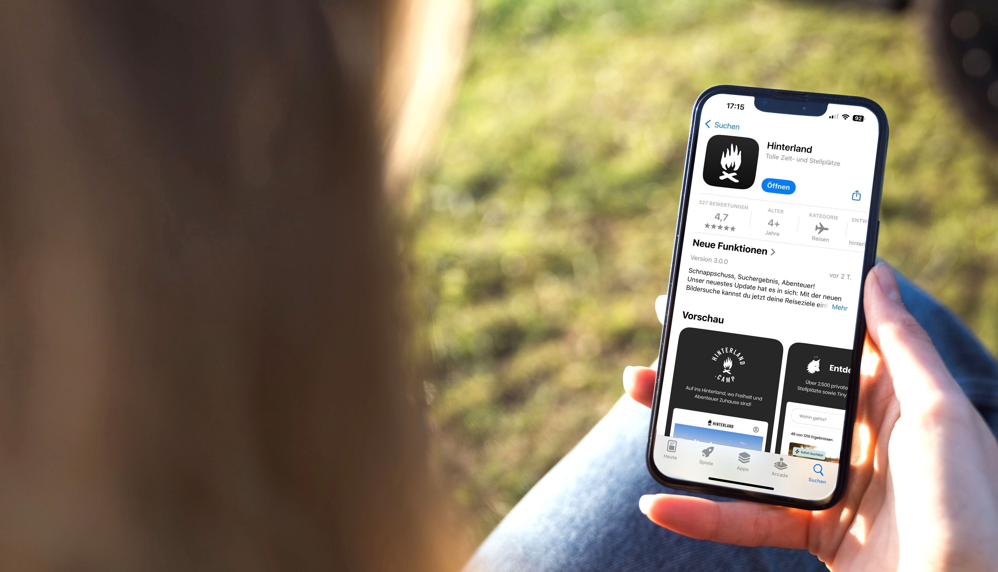 Eine Frau hält ein Handy in der Hand, auf dem die Hinterland-Camping-App im App-Store geöffnet ist.
