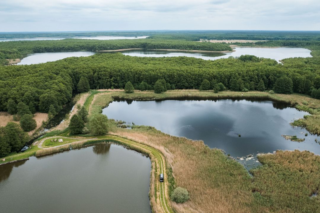 Camper fährt umgeben von Wasser auf einem kleinen Weg entlang der Seen des Müritz-Seen-Parks. Er befindet sich auf der Route des Roadtrips.