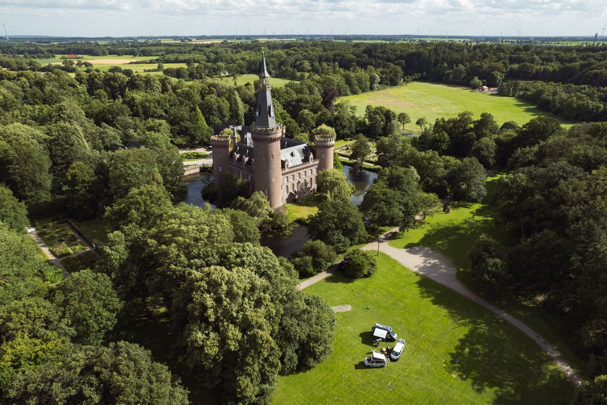 Drohnenfoto vom Schloss Moyland mit drei VW vans davor.
