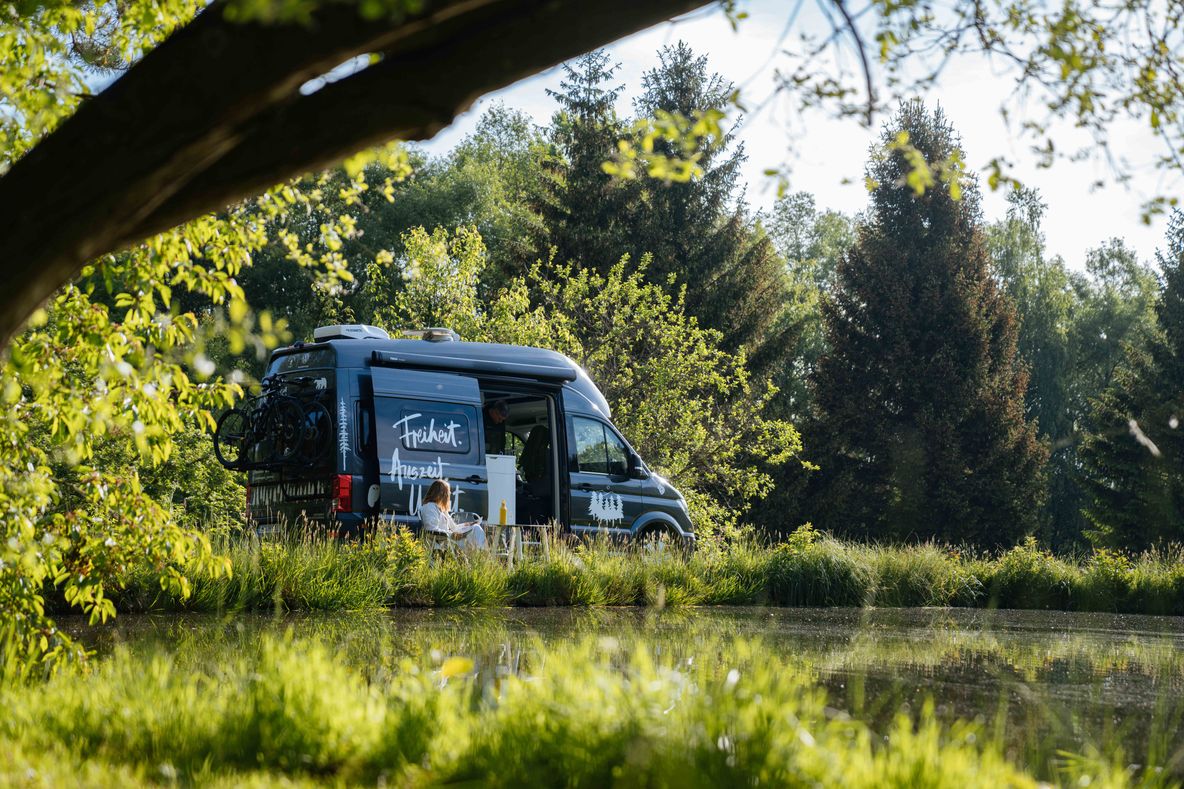 VW-Camper steht auf einem Stellplatz in Alleinlage an einem See von hinterland.camp