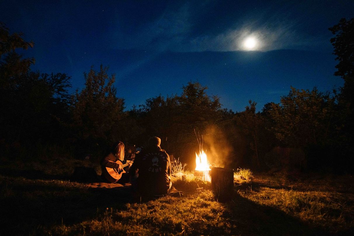 Das Hinterland-Team sitzt am Lagerfeuer an einer geeigneten Stelle auf einem privaten Camping Stellplatz in Alleinlage von hinterland.camp