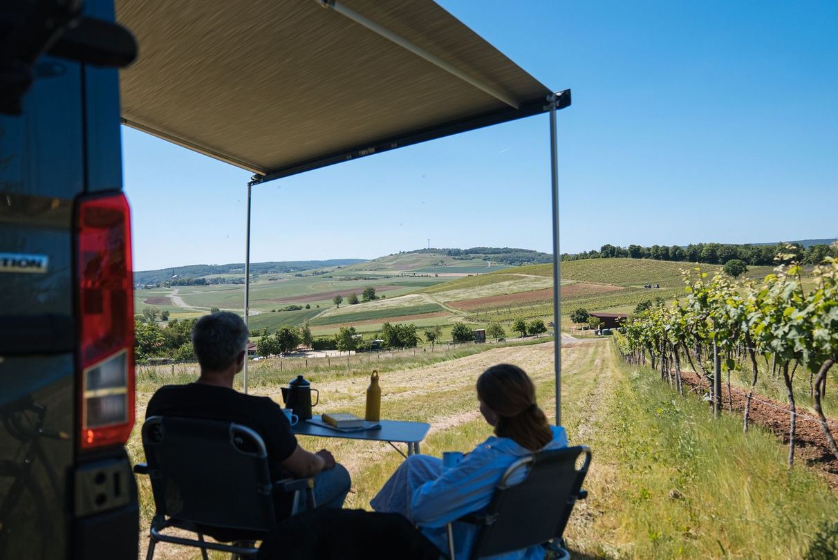 Camper steht auf einem Stellplatz in Alleinlage auf dem Berg eines Weinguts direkt neben den Weinreben mit Panoramablick auf die Felder, den Wald und die anliegenden Bauernhöfe