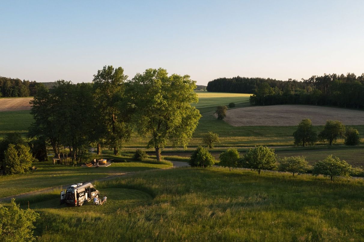 VW-Camper steht auf einem Stellplatz in Alleinlage von hinterland.camp umgeben von Feldern und Bäumen