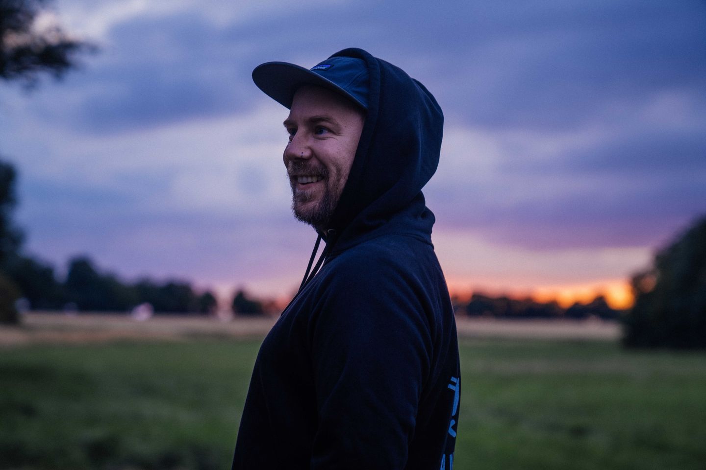 Steffen steht auf einer grünen Wiese bei Sonnenuntergang und lächelt nach links.