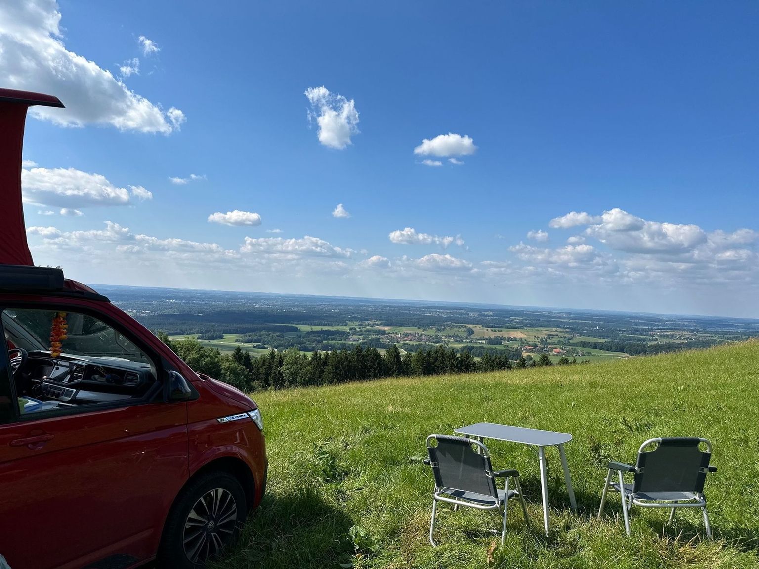 Camper steht auf einer Wiese mit Weitblick über die Berge Bayern. Die Wiese ist Teil eines Campingplatzes in Bayern von hinterland.camp.