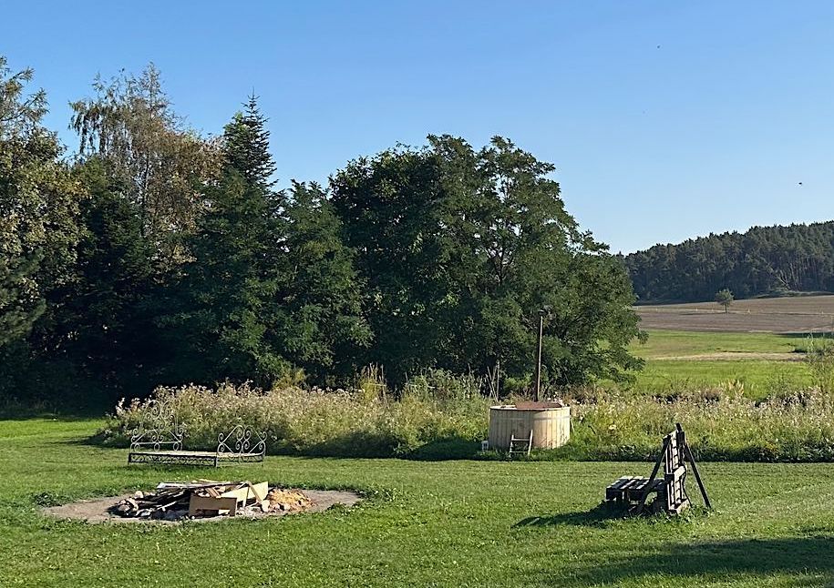 Stellplatz mit einer Feuerstelle, einem Whirlpool und einer handgefertigten Bank an der Feuerstelle. Der Stellplatz ist Teil eines Wellness-Campingplatzes von hinterland.camp.