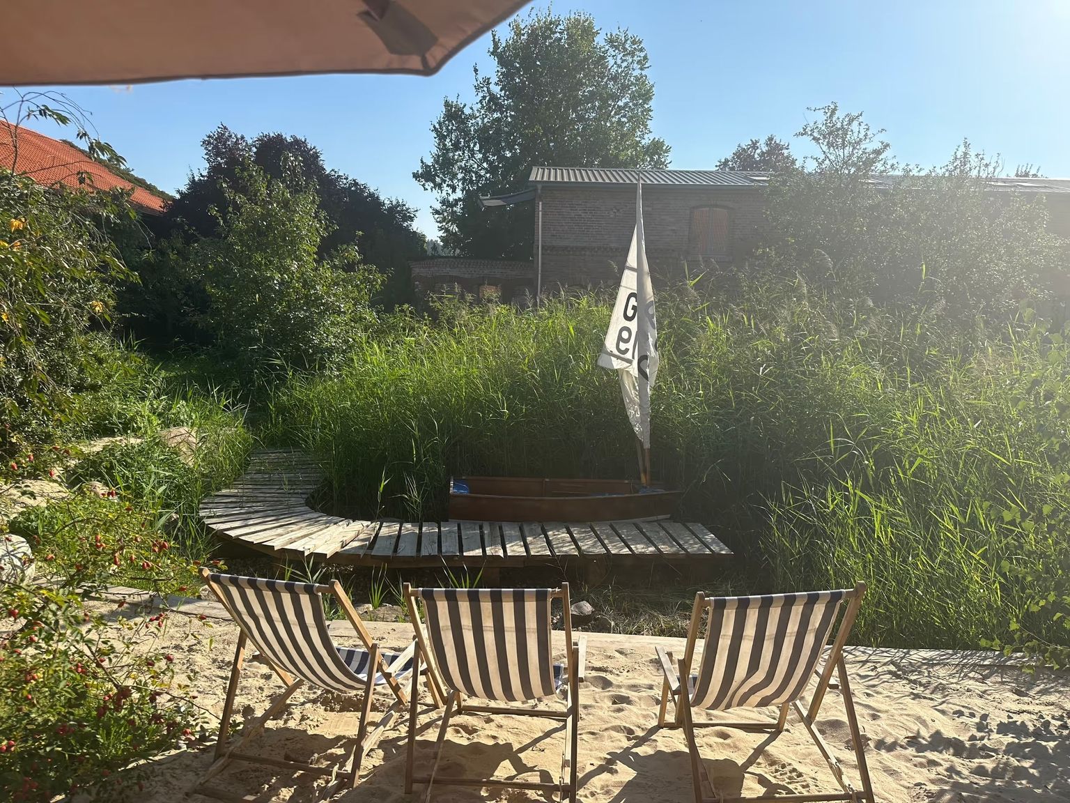 Nett angelegter Strand des Wellness-Camps von hinterland.camp mit Liegestühlen und einem Sonnenschirm