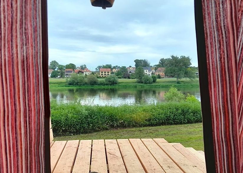 Blick aus einem Holz-Shelter auf die Elbe. Die Gardinen sind im Vordergrund zu sehen.