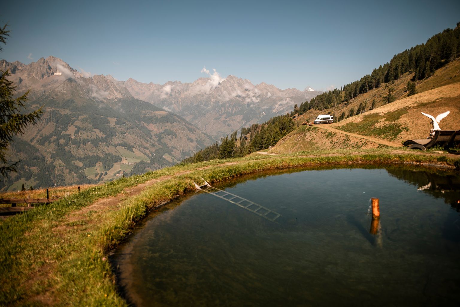 Camper steht auf einem Panorama-Stellplatz umgeben von Alpen und einem kleinen Teich