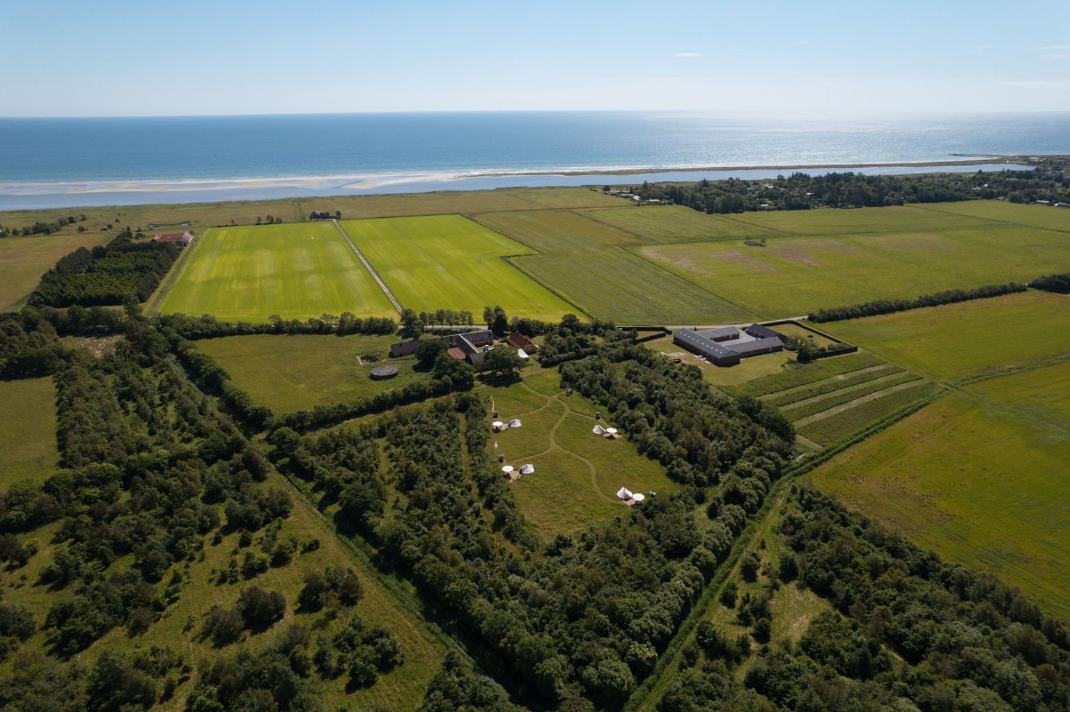 Drohnenaufnahme eines Grundstückes direkt am Meer in Dänemark, auf dem Glampingzelte zur Übernachtung stehen. Die Übernachtung kann man auf hinterland.camp buchen.