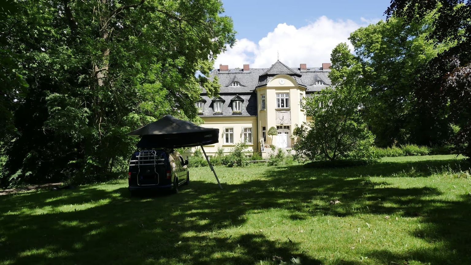 Camper steht auf einem idyllischen Stellplatz vor einem Gutsahof auf einem Wellness-Campingplatz von hinterland.camp