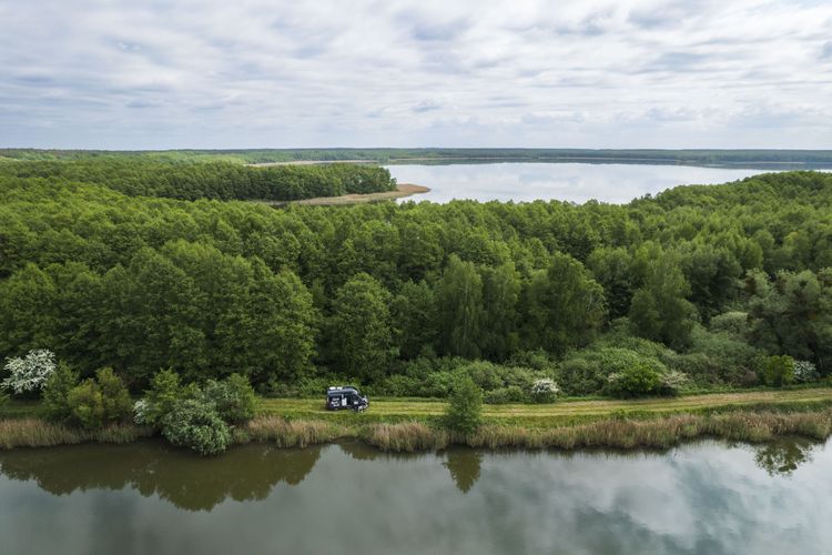 Camper steht auf einem Stellplatz von privat von hinterland.camp in Alleinlage in einer Seenlandschaft an der Müritz umgeben von grünen Wiesen, Wald und Wasser
