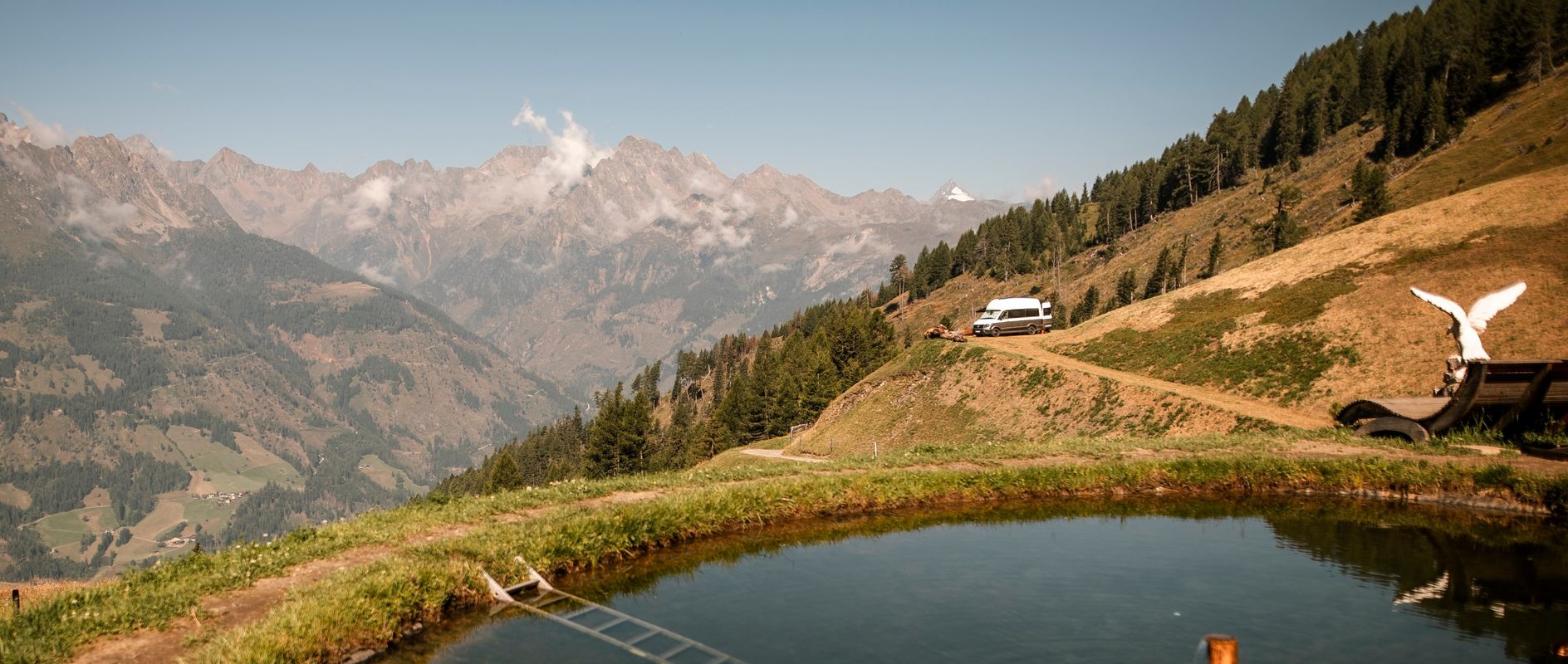 Ein VW-Camper steht auf einem privaten Stellplatz an der Alm mit einem unfassbar weitem Blick in die Alpen.