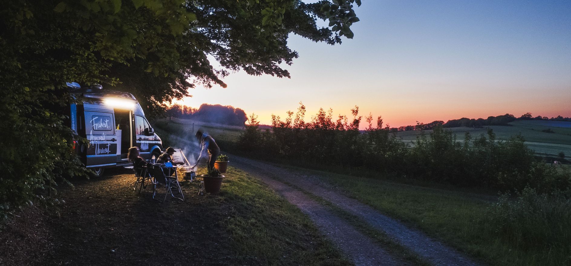 Ein Camper steht bei Sonnenuntergang auf einem naturnahem Camping-Stellplatz in Dresden.