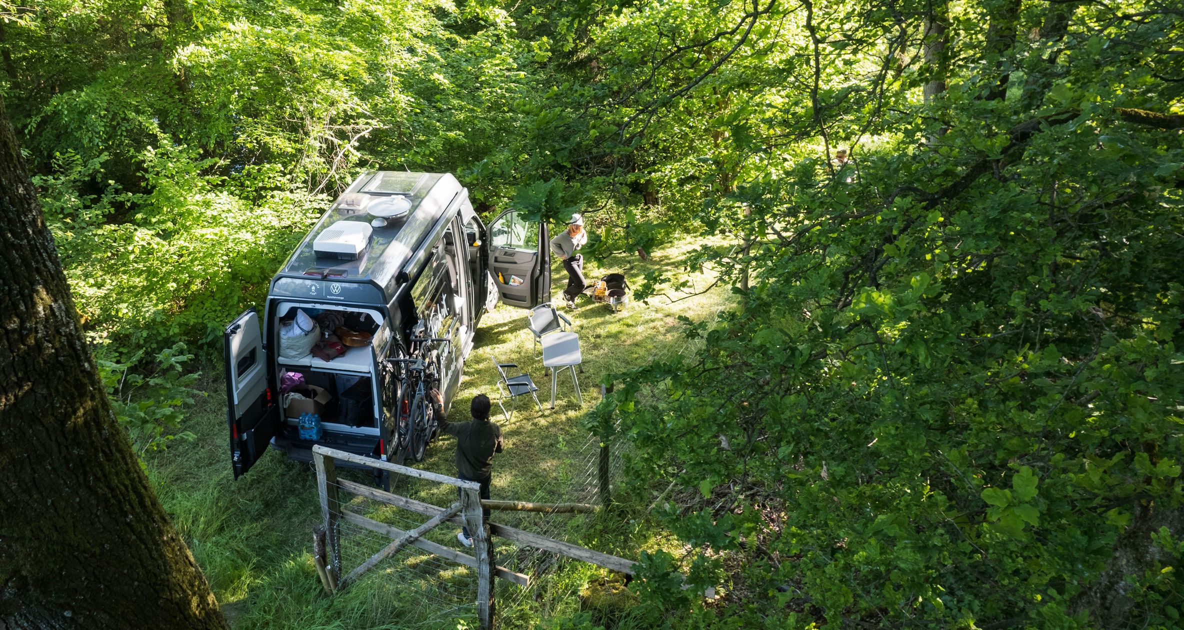 VW-Camper steht auf einem Naturcampingplatz geschützt zwischen Bäumen im Wald, mitten in der Natur