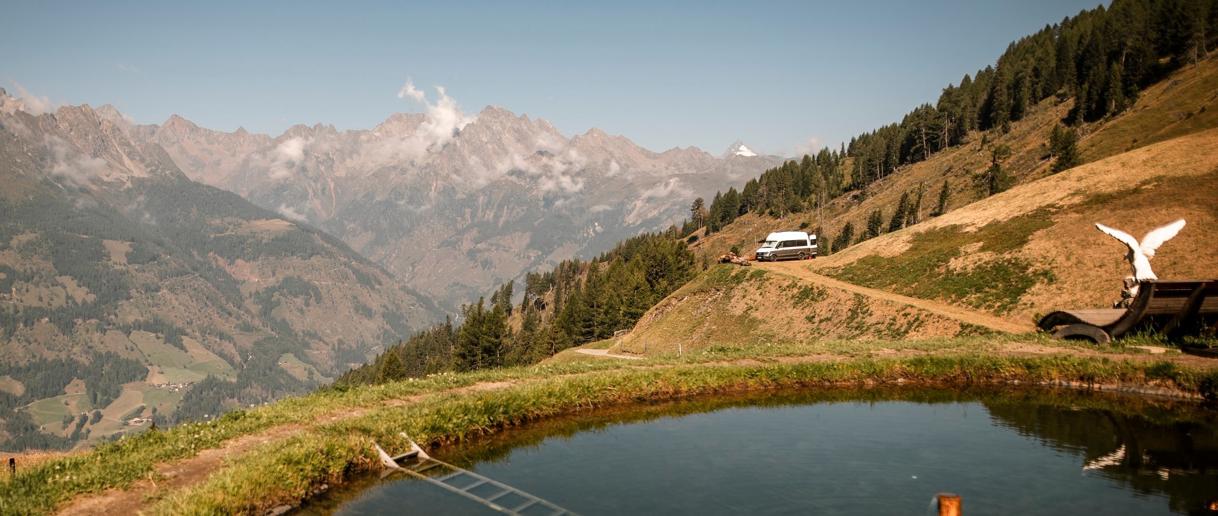 Ein VW-Camper steht auf einem privaten Stellplatz an der Alm mit einem unfassbar weitem Blick in die Alpen.