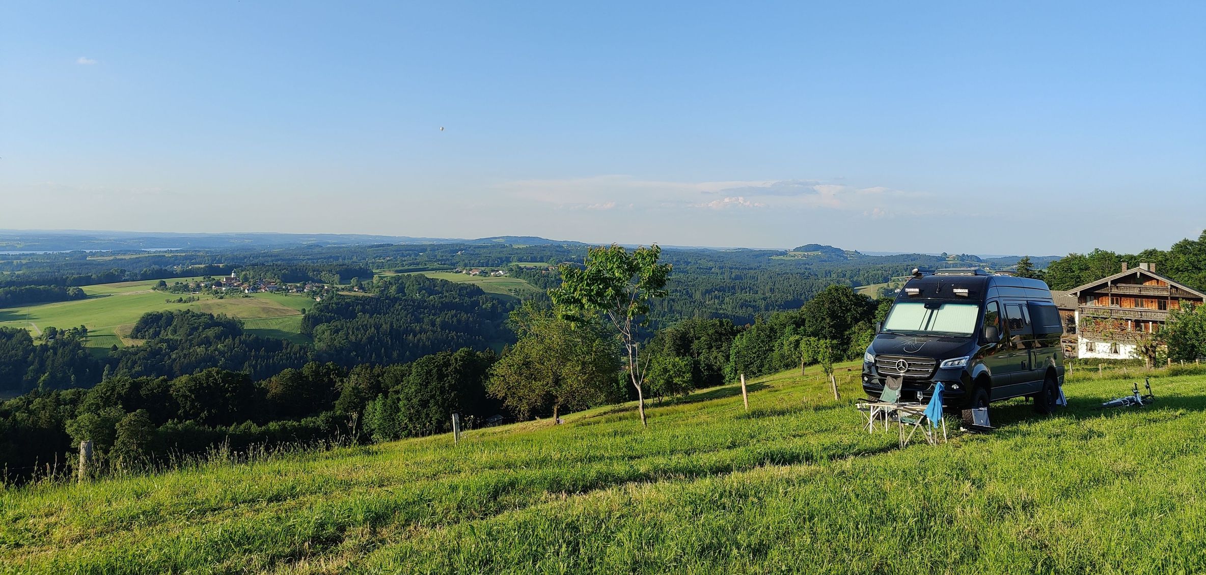 Ein Camper steht auf einer privaten Wiese, einem Minicamping von hinterland.camp. Im Hintergrund sieht man die Berghütte der Gastgeber:Innen und ein wunderschönes Panorama über die Berge.