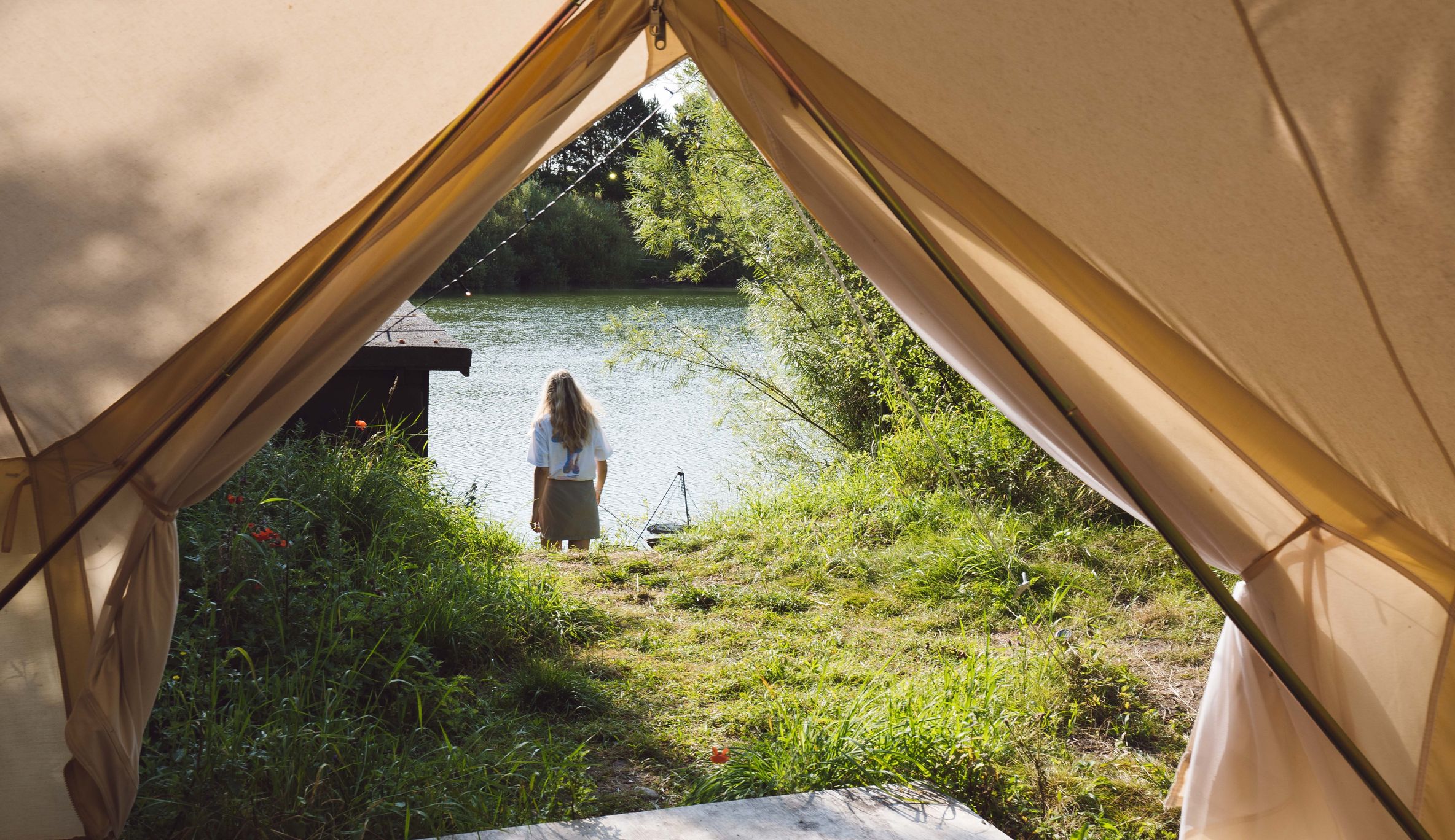 Eine Frau geht zum Wasser eines Sees in Dänemark. Der Fotograf steht in einem Glampingzelt, der Eingang des Zeltes ist noch angeschnitten zu sehen.