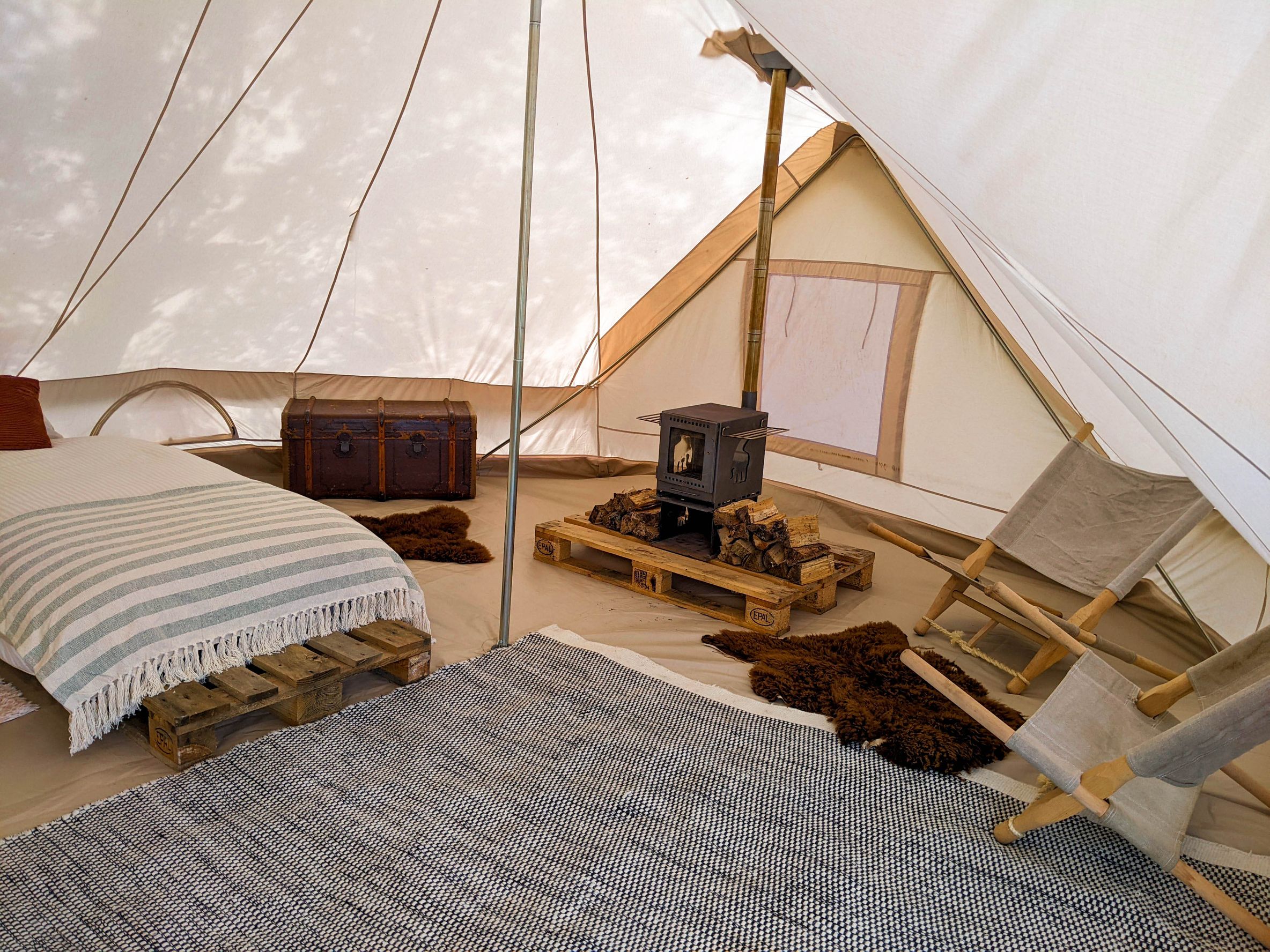Glamping-Zelt mit Kamin, Liegestühlen und Betten von innen, buchbar bei hinterland.camp
