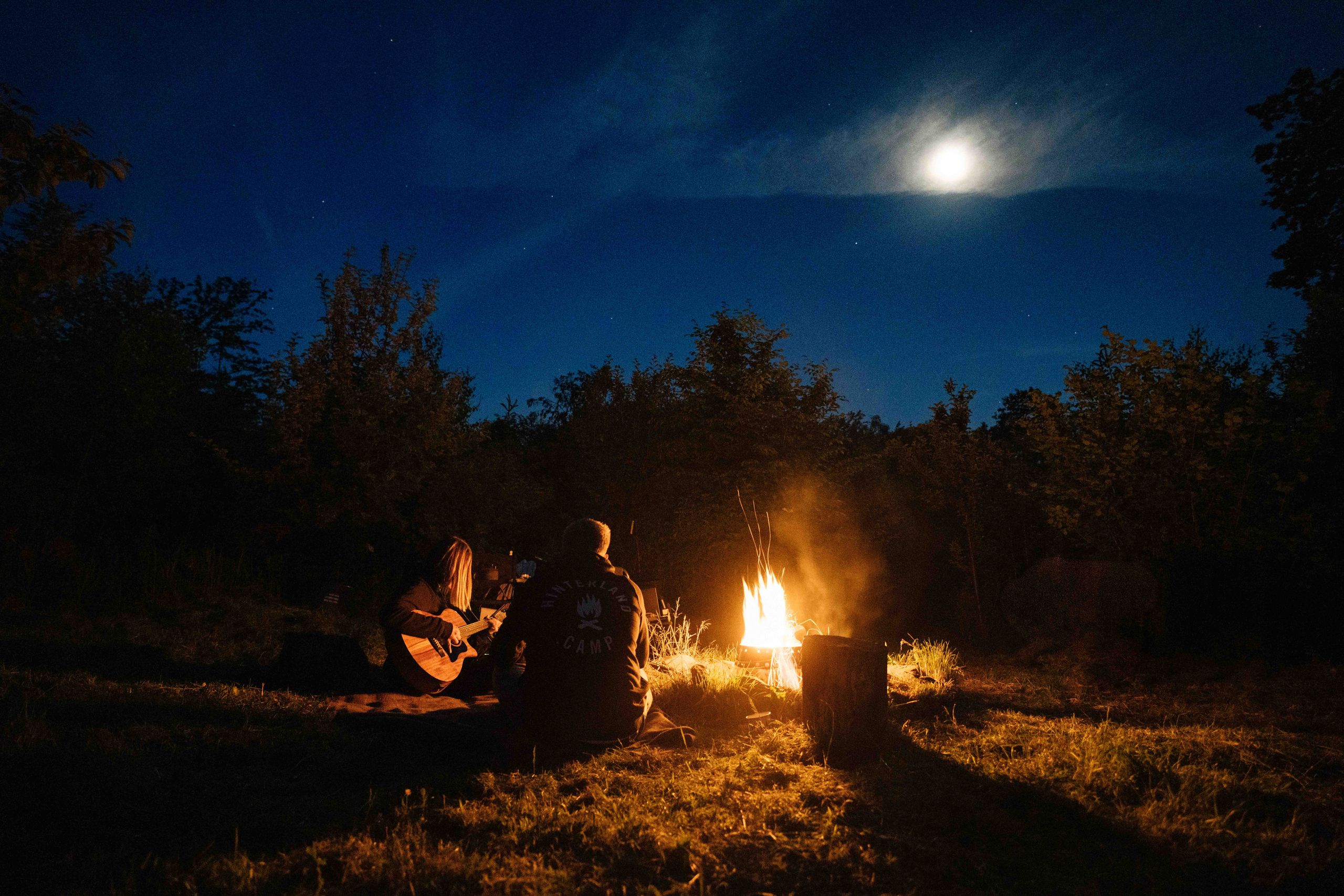 Das Hinterland-Team sitzt am Lagerfeuer an einer geeigneten Stelle auf einem privaten Camping Stellplatz in Alleinlage von hinterland.camp