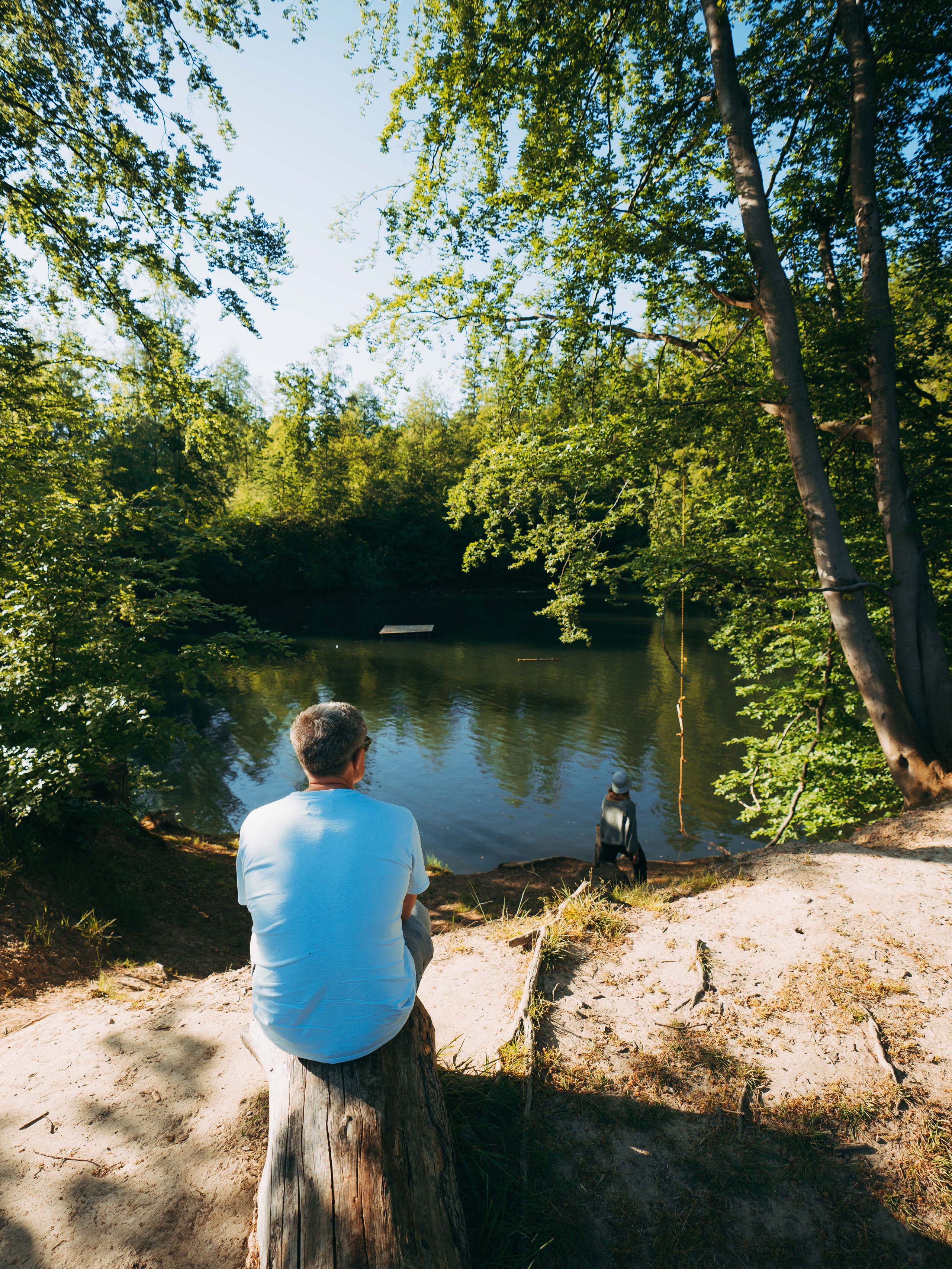 Mann sitzt an einem privaten See eines Camping-Stellplatzes, der über hinterland.camp gebucht wurde