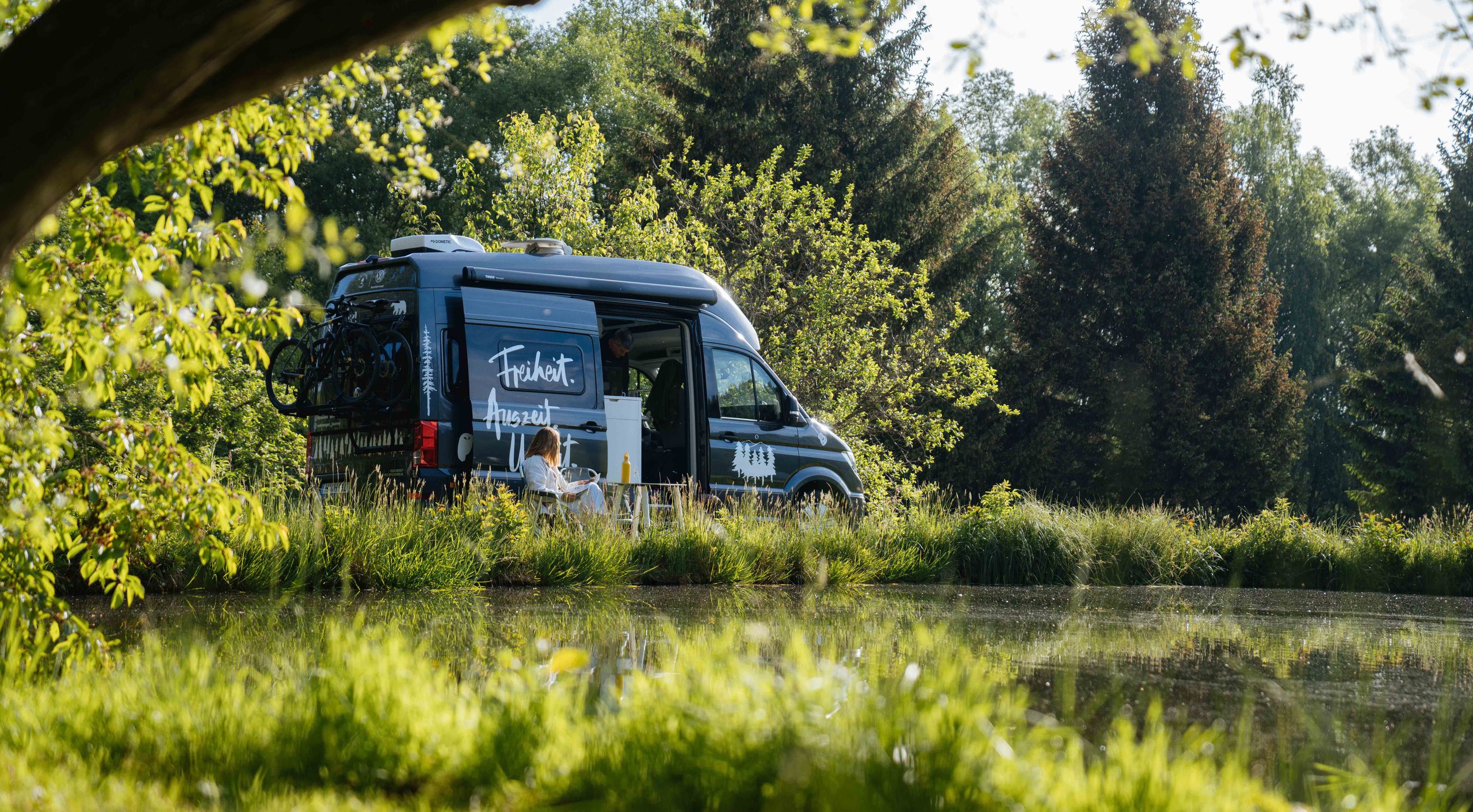 VW-Camper steht auf einem Stellplatz in Alleinlage an einem See von hinterland.camp