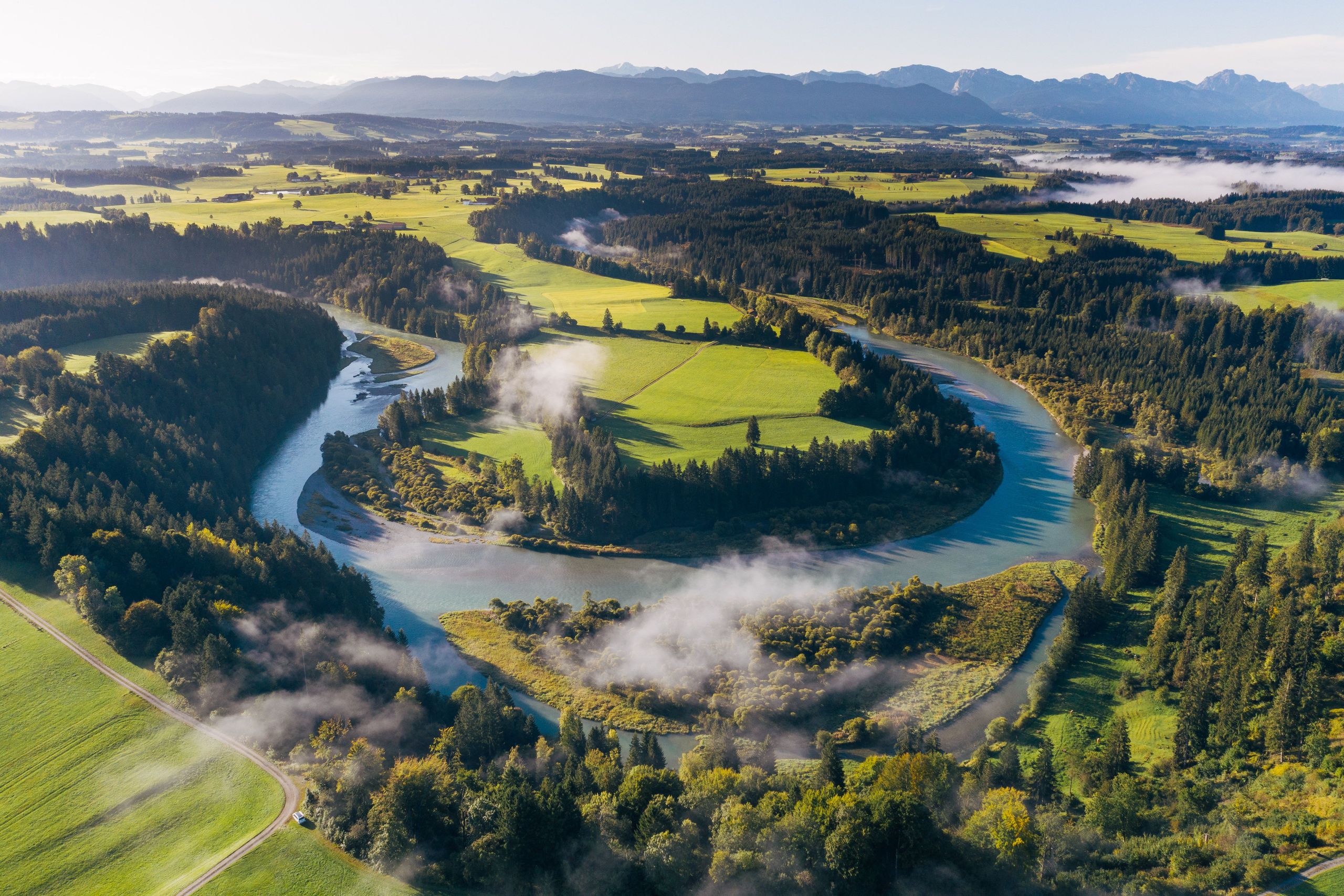 Drohnen-Aufnahme eines Flusses umgeben von Wald und grünen Wiesen