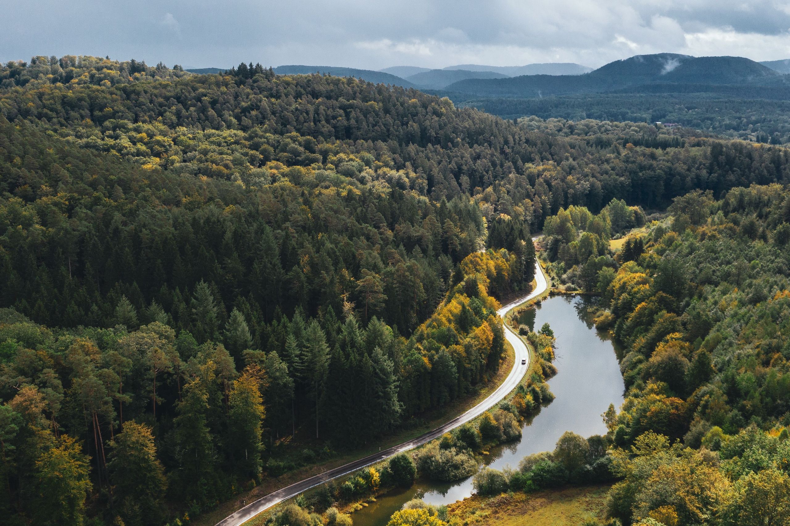 Drohnen-Aufnahme einer Straße entlang eines Flusses im bewaldeten Gebirge