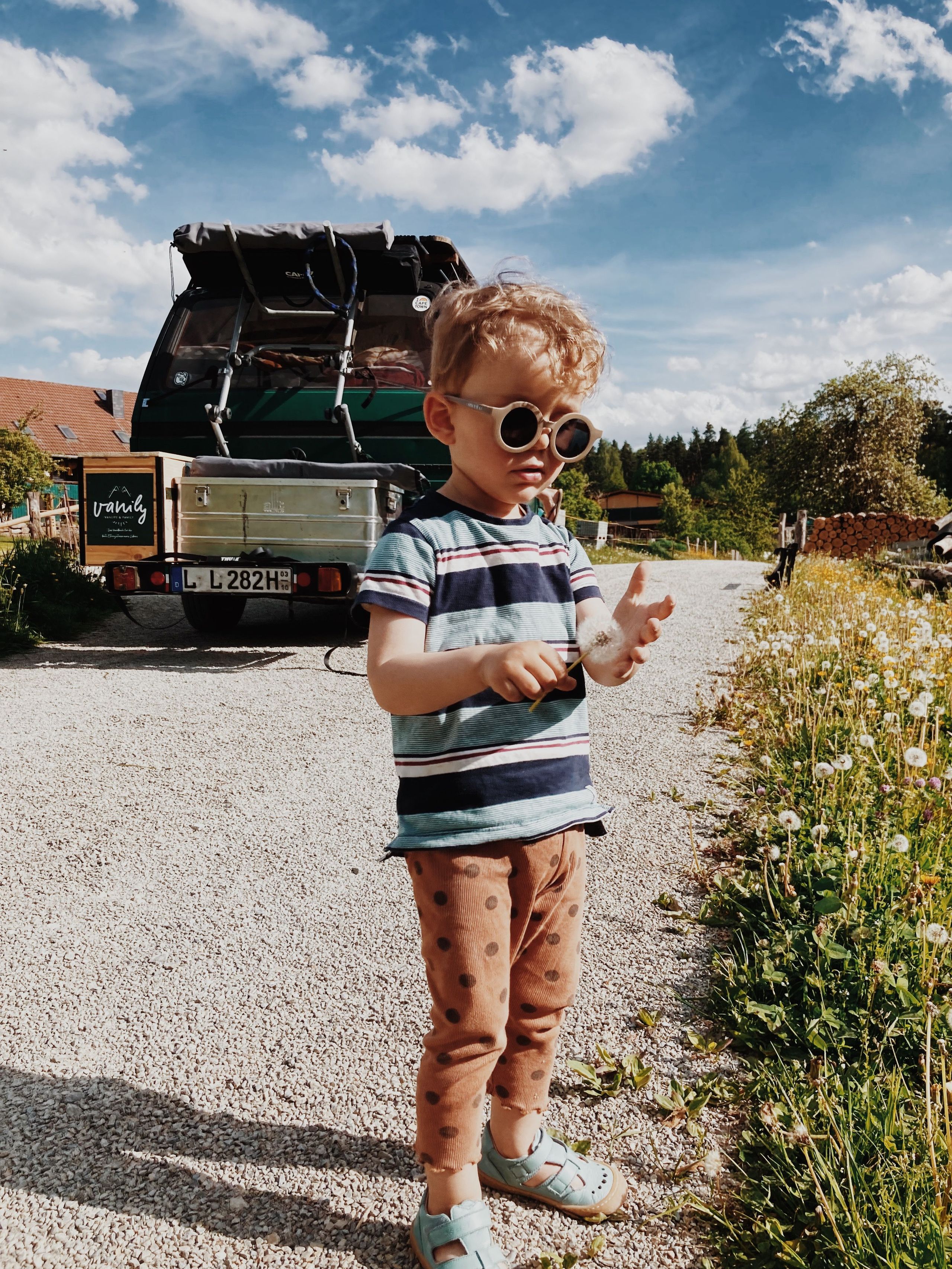 Ein Kind steht vor einem VW-Camper mitten im Grünen auf einem Naturcamping Stellplatz von hinterland.camp