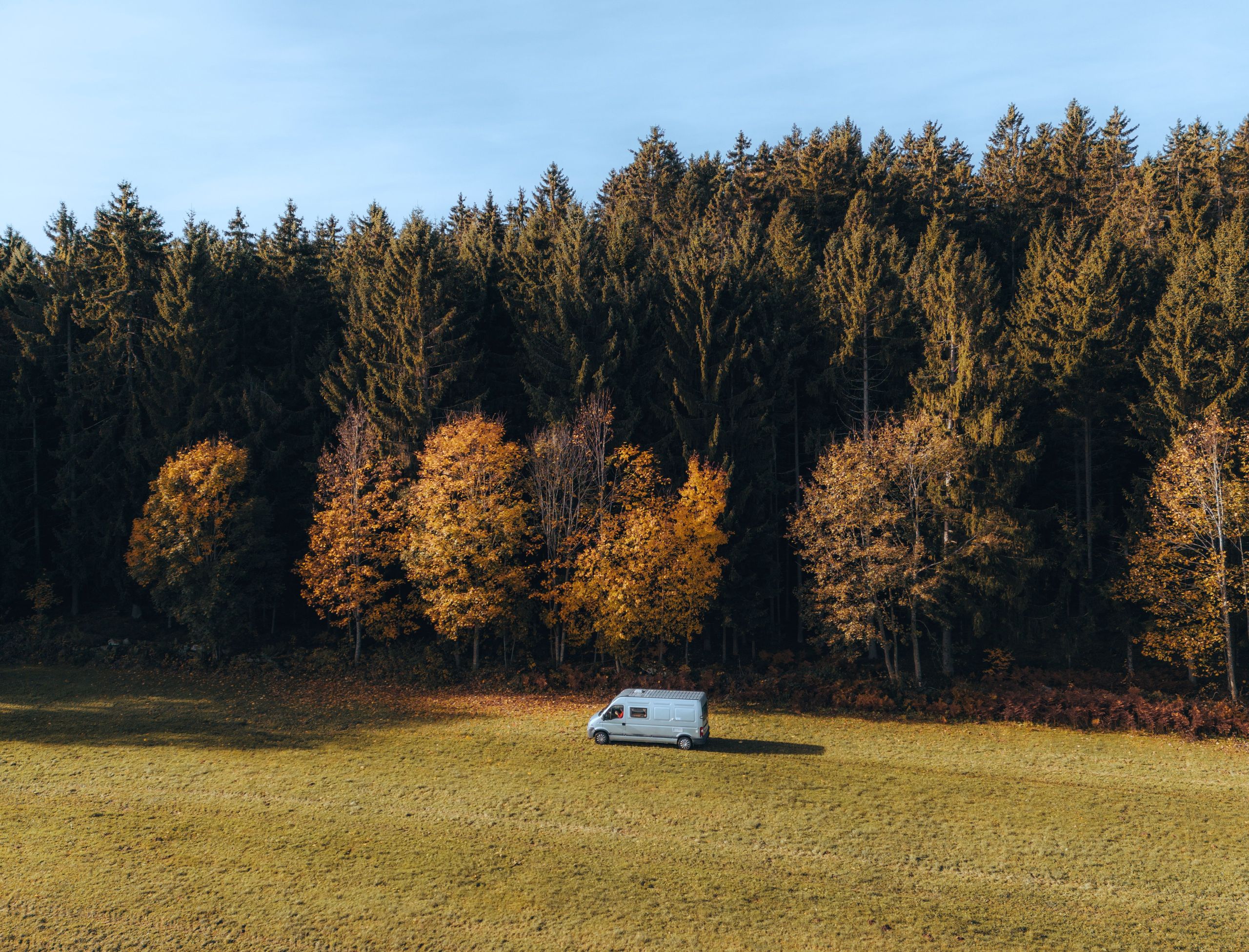 Ein Camper steht auf einer riesigen Wiese direkt am Waldrand in Bayern ganz allein. Den Stellplatz kann man bei hinterland.camp buchen.