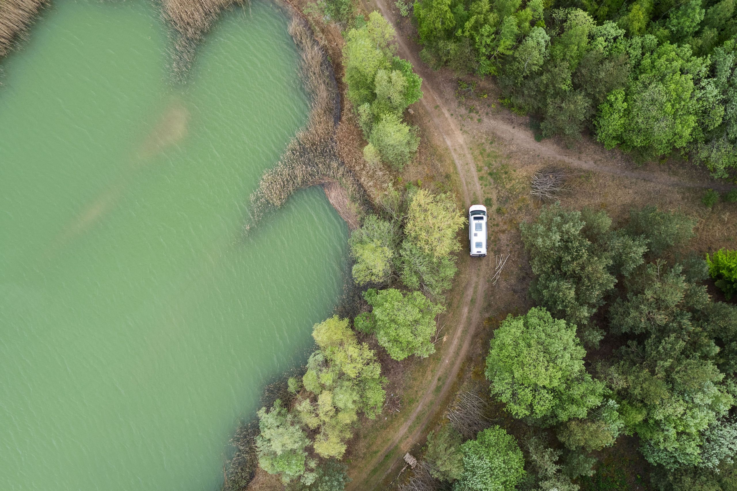 Drohnen-Aufnahme Camper fährt auf einer Straße entlang eines Sees und Waldes