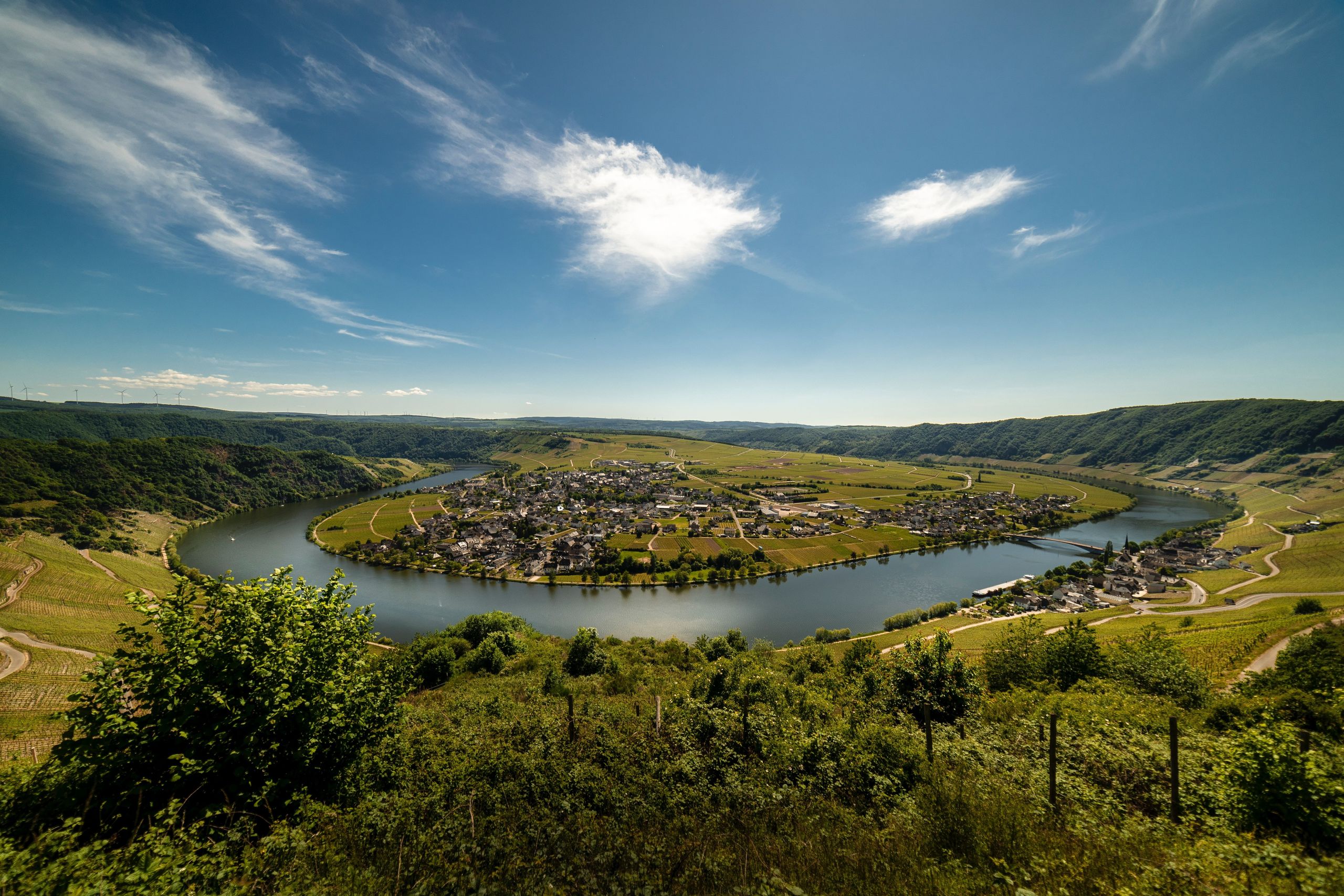 Mosel verläuft in einer Schlaufe entlang eines kleinen Dorfes umgeben von Wiesen, Wäldern und Bergen