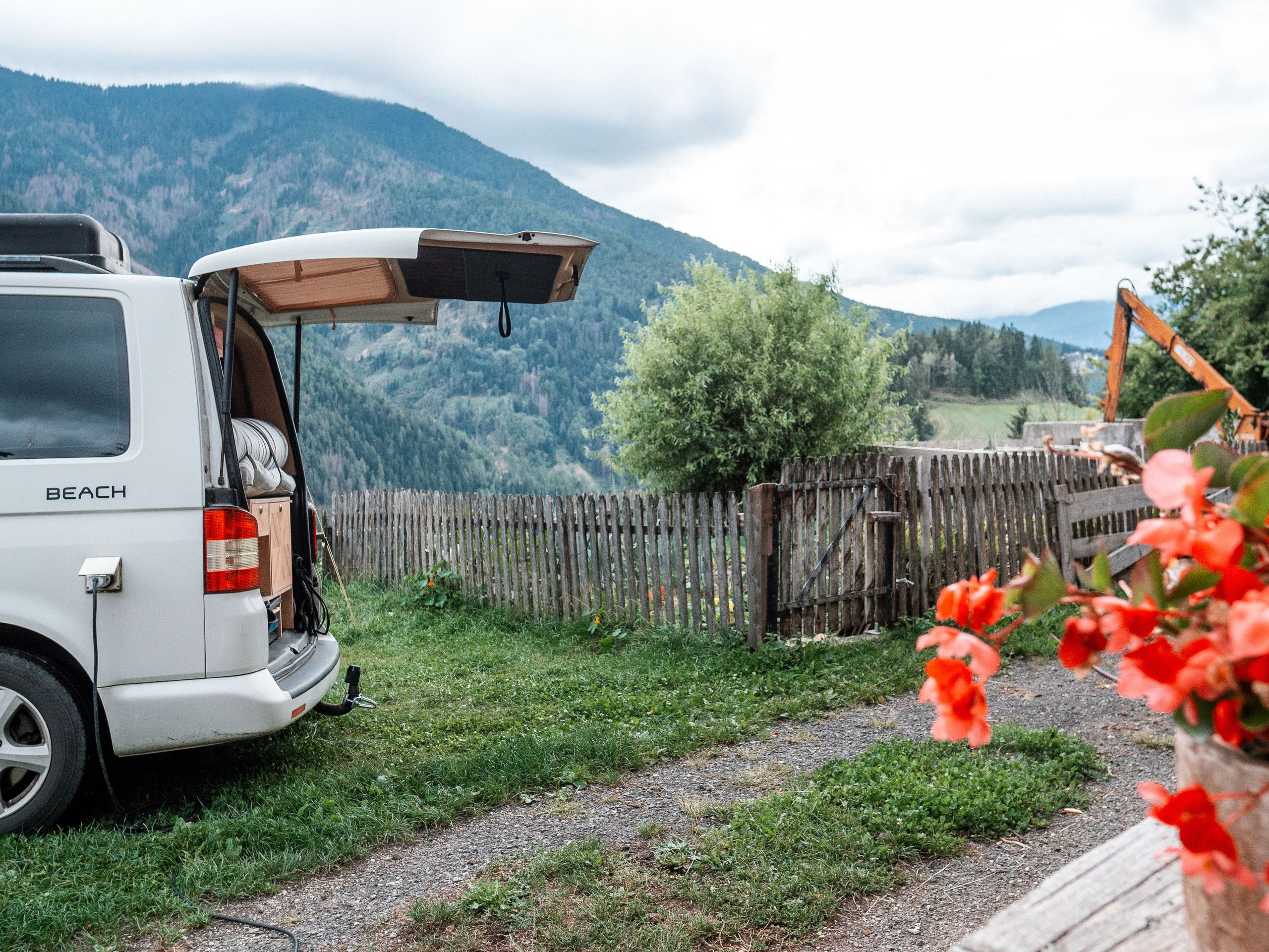 Ein VW-Camper steht mitten im Gebirge vor einem Tal mit wunderschönen roten Blumen im Vordergrund. Es befindet sich auf einem Wildcamping-Stellplatz von Hinterland.