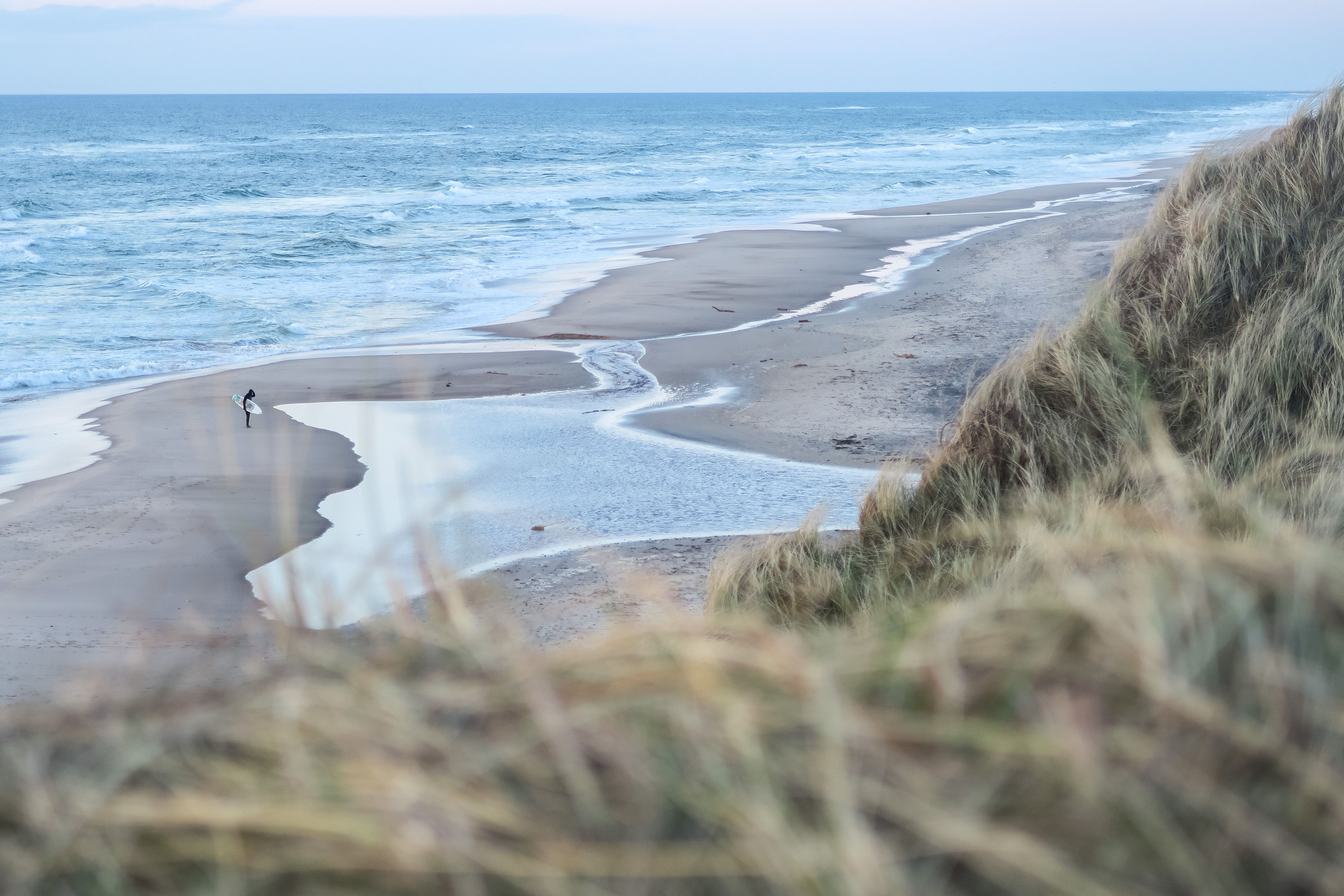 Ein Surfer läuft mit seinem Surfboard über einen Strand an der Nordsee