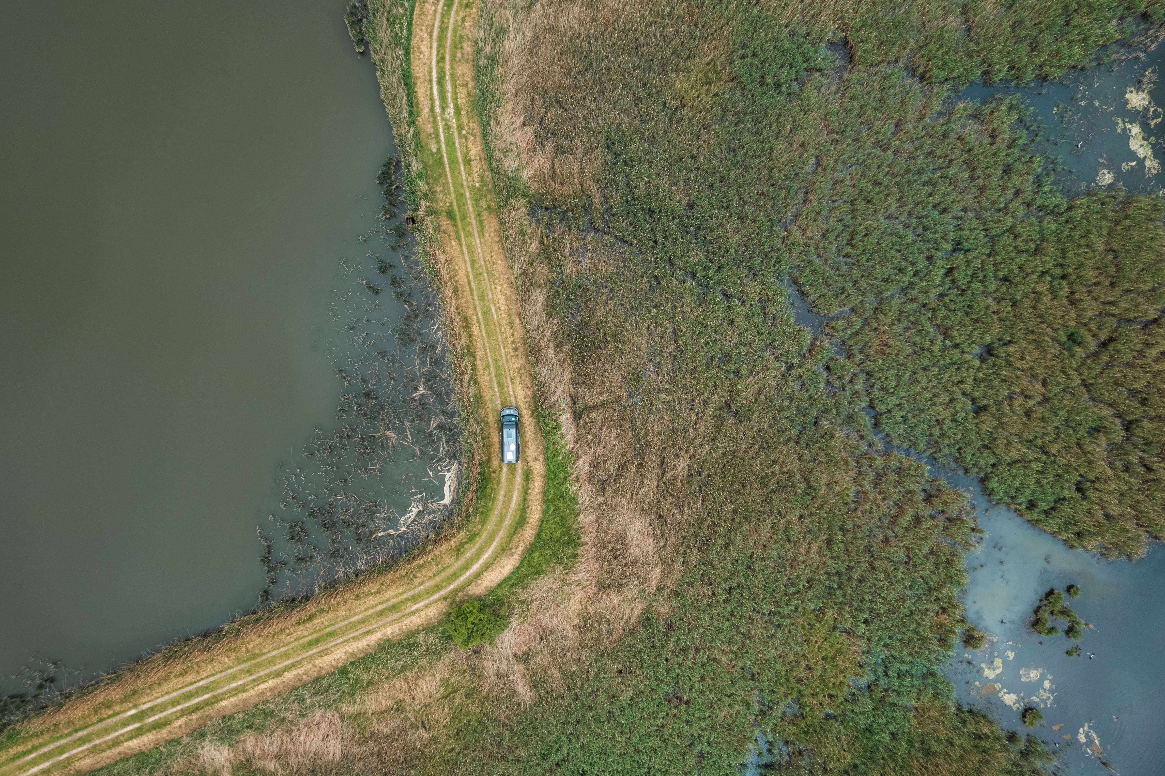 Camper Van fährt über eine Straße umgeben von Wasser auf zu einem Stellplatz am Wasser in Alleinlage von hinterland.camp