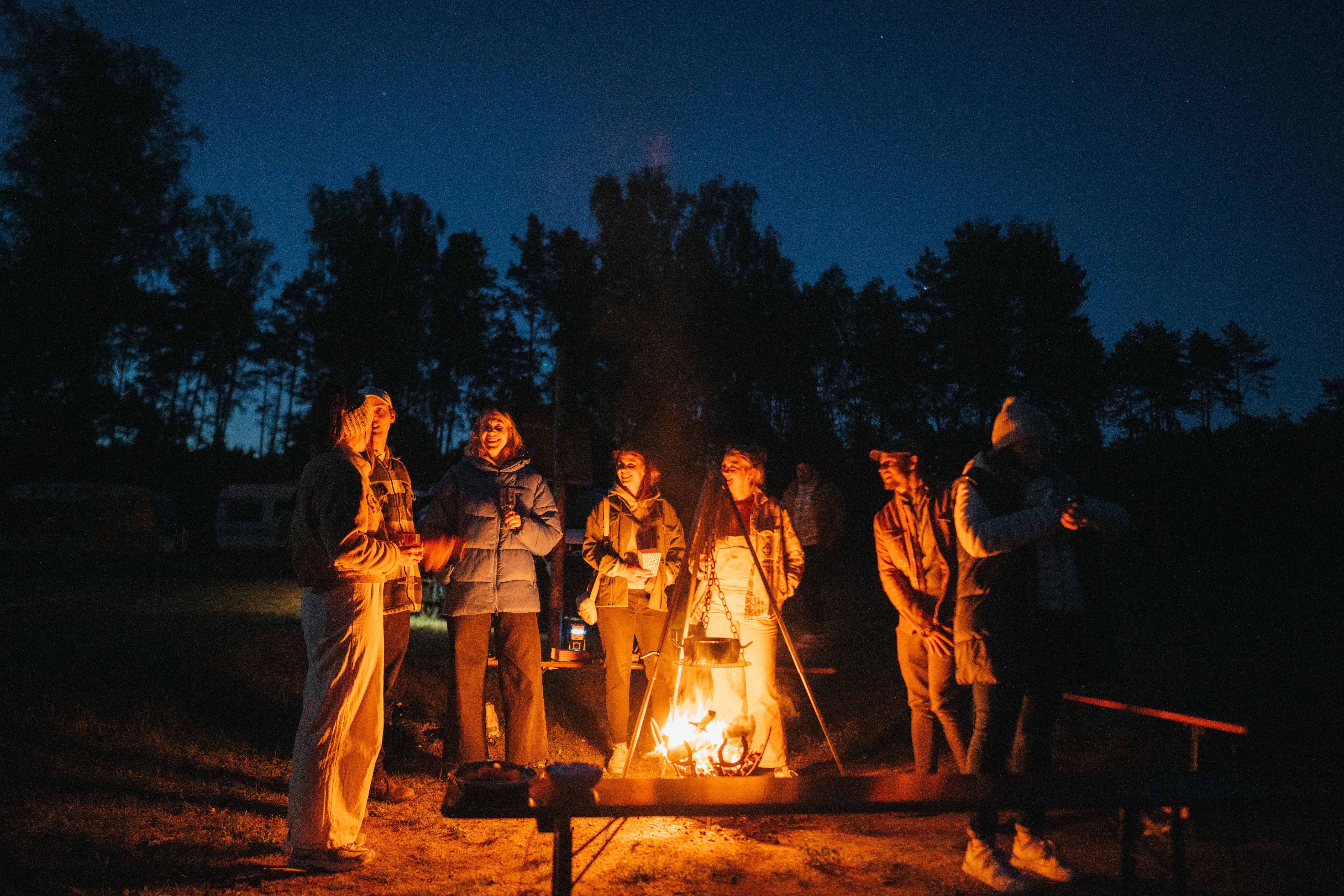 Menschen stehen um ein wärmendes Lagerfeuer herum, unterhalten sich und lachen