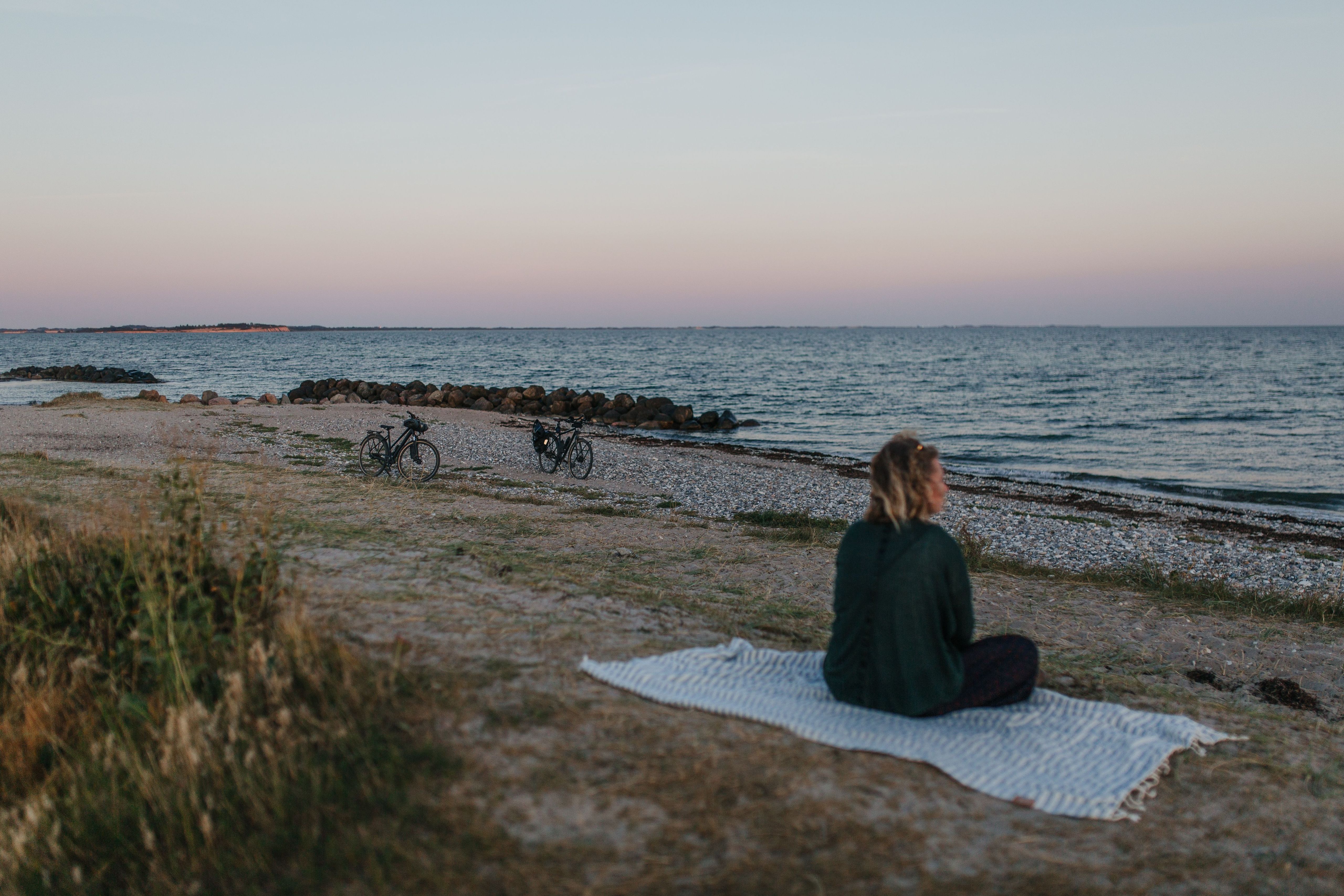 Frau in der Abendsonne am Strand mit Fahrrädern. Sie befindet sich bei einem Tiny House direkt am Strand, welches man über hinterland.camp buchen kann.