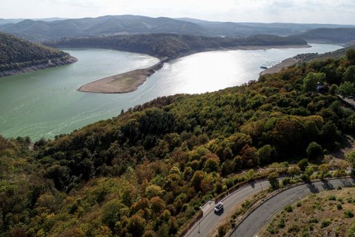 Vogelperspektive auf den Rhein umgeben von Wäldern und Bergen, Camper / Van fährt auf einer Serpentinen-Straße