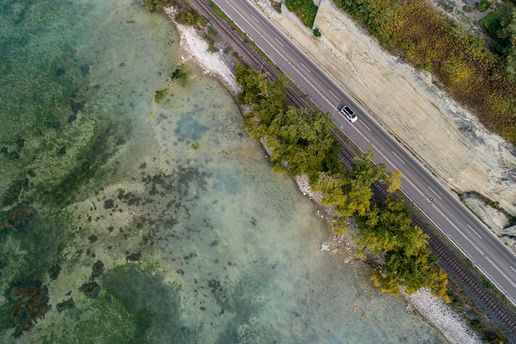 Van fährt auf einer Straße am Rand des Bodensees, Man kann das Wasser, einen Strand, Bäume und Dünen erkennen