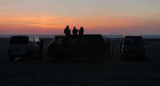 3 Bulli stehen direkt am Strand der Ostsee in Schleswig Holstein. Drei Menschen sitzen auf der Dachterasse eines T3 Campers direkt am Strand in Alleinlage