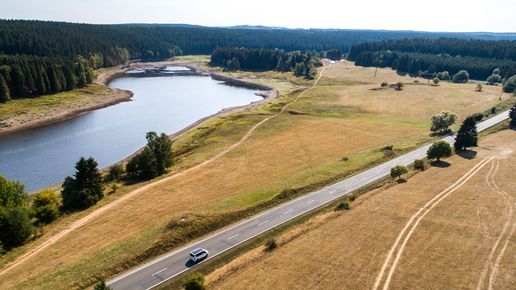 Camper fährt auf einer Straße Estland eines Flusses, umgeben von Stoppelfeldern und Wald