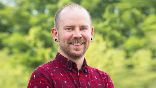 Steffen lacht in die Kamera vor leuchtend grünen Bäumen