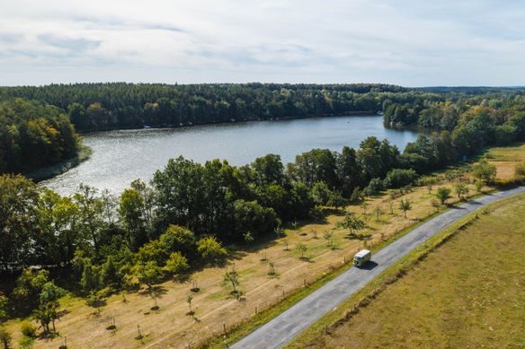 Camper Van fährt in Brandenburg über eine Straße entlang eines Sees umgeben von Natur, Wäldern, grünen Wiesen