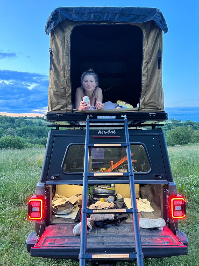 Eine Frau liegt im Dachzelt auf einem Camper. Das Fahrzeug steht auf einem Campingplatz bei Dresden, den man auf hinterland.camp buchen kann.