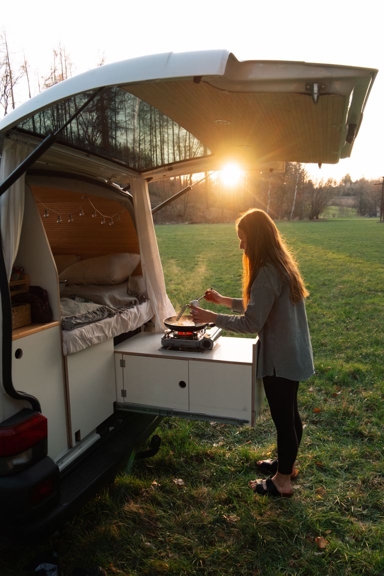 Frau kocht auf ausziehbarer Campingküche am Kofferraum eines Campers