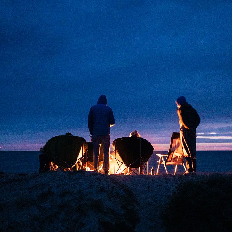 Gruppe am Lagerfeuer bei Sonnenuntergang mit Meer im Hintergrund