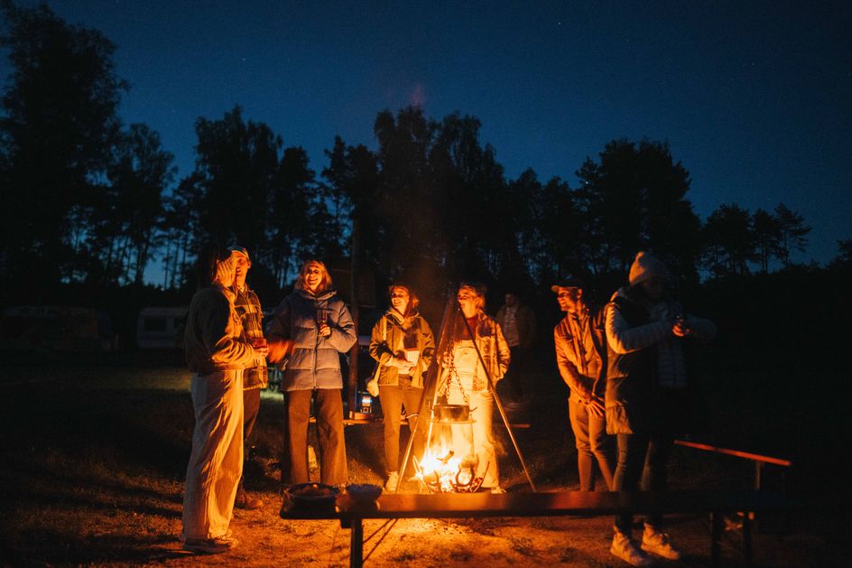 Menschen stehen um ein wärmendes Lagerfeuer herum, unterhalten sich und lachen